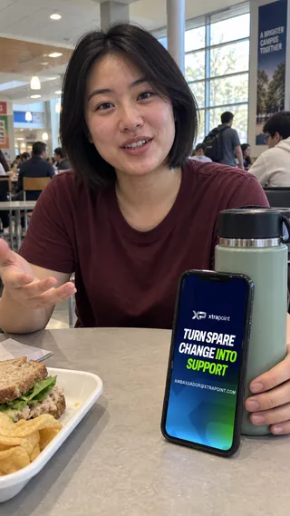 Ambassador content mockup of a student at a cafeteria table with the XtraPoint page on a phone.